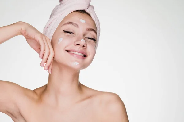 Ευτυχισμένη γυναίκα με μια πετσέτα στο κεφάλι της κρέμα εφαρμόζεται στο δέρμα του προσώπου — Φωτογραφία Αρχείου