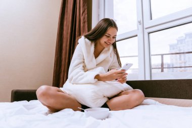 bornoz yatakta oturuyor ve seyir telefon içinde mutlu kadın