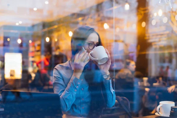 woman sitting outside the window drinking tea and talking on the phone