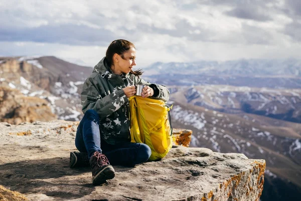 Mujer turista se sienta y bebe té sobre el fondo de las altas montañas —  Fotos de Stock