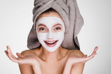 Kafasındaki bir havlu ile mutlu kadın yüz cilt temizlemek için bir maske uygulanan