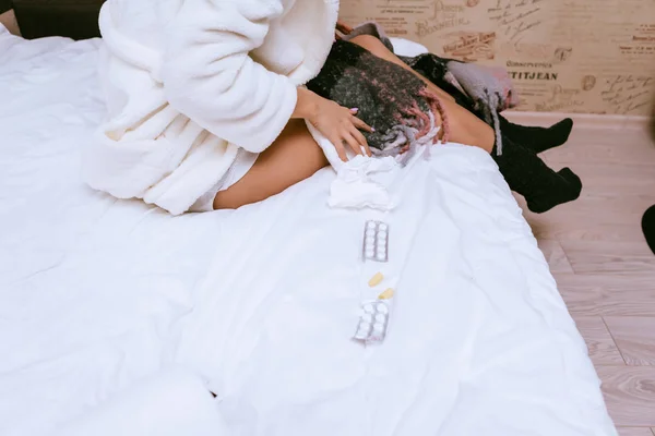 Ένα κορίτσι σε μια ρόμπα λευκό terry είναι κάθεται στο κρεβάτι, άρρωστος, που βρίσκεται δίπλα από το χάπι — Φωτογραφία Αρχείου