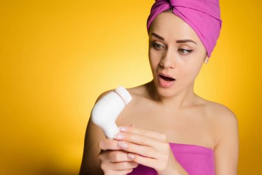 yüz cilt temizliği için elektrikli bir fırça tutan başında pembe havlu ile sürpriz genç kız