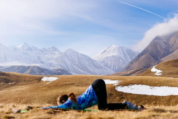 Активная девушка в синей куртке, занимающаяся йогой на фоне Кавказских гор — стоковое фото