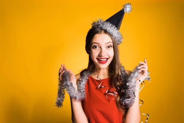 Happy νεαρό κορίτσι στο Χριστουγεννιάτικο καπέλο γιορτάζει τα Χριστούγεννα, στο λαιμό ασημένια στολίδια — Φωτογραφία Αρχείου