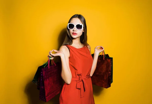 Uma menina atraente em um vestido vermelho e óculos de sol comprou muitos presentes em uma sexta-feira preta — Fotografia de Stock