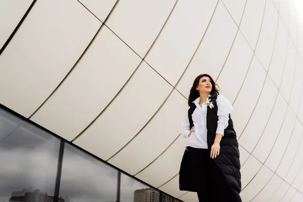 Стильная молодая женщина в черном костюме позирует на фоне необычной архитектуры города Баку — стоковое фото