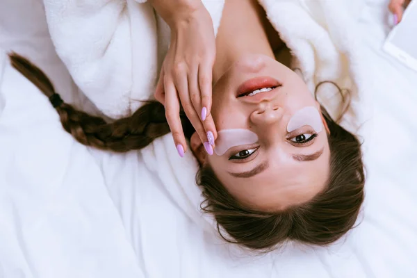 귀여운 웃는 소녀 흰색 패치 눈 아래 침대에 거짓말 — 스톡 사진