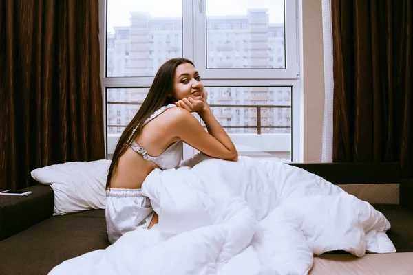 Mujer feliz se sienta en la cama debajo de una manta — Foto de Stock