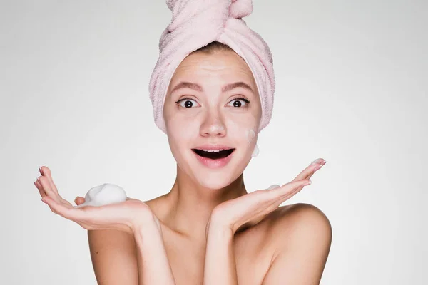 Happy woman with a towel on her head after a shower holds a foam in her hand — Stock Photo, Image