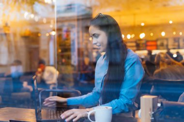 pencerenin dışında kadın masada oturur ve laptop görünüyor