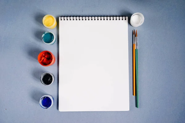 Foglio bianco di carta su uno sfondo di vernici colorate e pennelli — Foto Stock