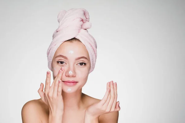 Удивленная женщина с полотенцем на голове наносит крем на кожу лица — стоковое фото