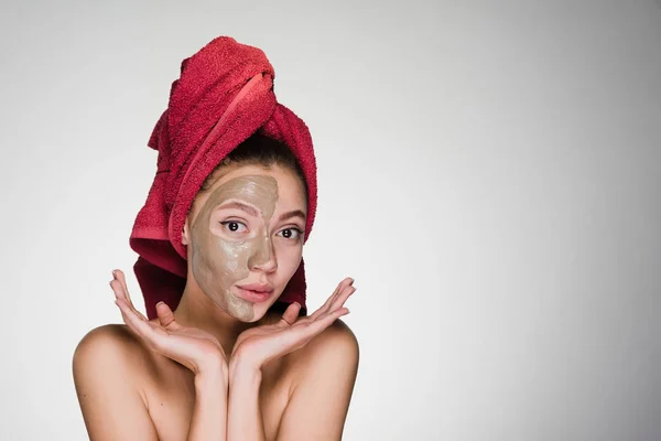 Μια έκπληξη γυναίκα με μια πετσέτα στο κεφάλι της μια μάσκα εφαρμόζεται στο δέρμα του προσώπου της — Φωτογραφία Αρχείου