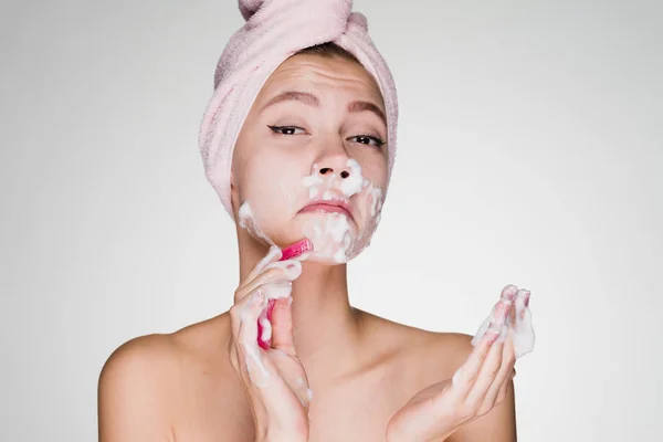 Frau mit einem Handtuch auf dem Kopf nach der Dusche macht eine Gesichtsenthaarung mit einem Rasierer — Stockfoto