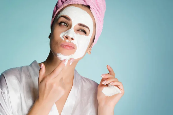 Una mujer con una toalla en la cabeza después de la ducha se aplica una máscara limpiadora en la cara —  Fotos de Stock