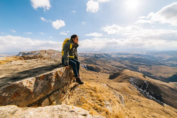 Woman tourist with a backpack sits on the background of mountains — Stock Photo, Image