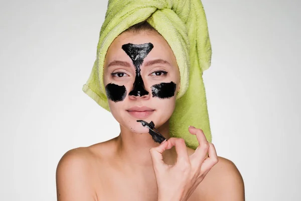 A woman with a towel on her head removes the mask from her face — Stock Photo, Image