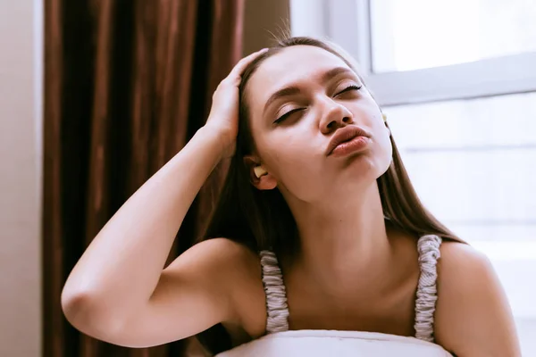 Sleepy vrouw zit op het bed op de achtergrond van windows — Stockfoto