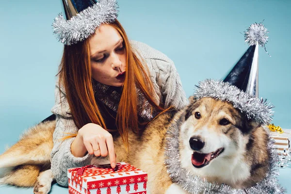 Mujer feliz en una gorra festiva se sienta al lado de un perro grande sobre un fondo de regalo — Foto de Stock