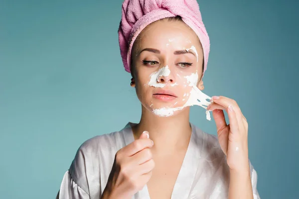 Женщина с полотенцем на голове снимает очищающую маску с кожи лица — стоковое фото