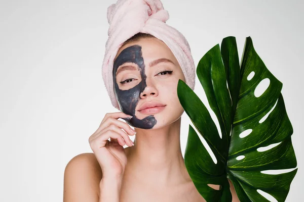 A woman with a towel on her head after showering put a mask on her face and holds a green leaf — Stock Photo, Image