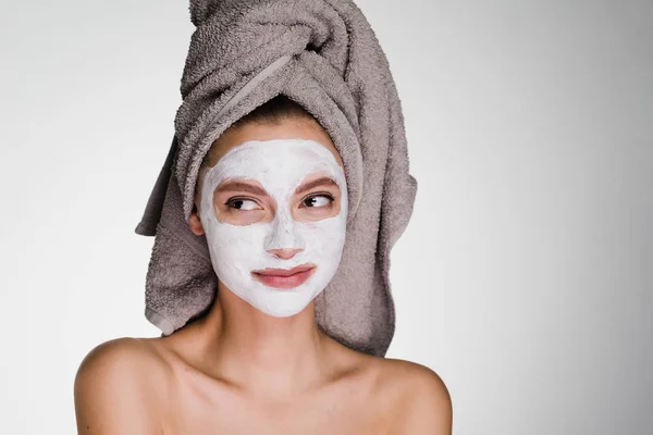 Вдумчивая женщина с полотенцем на голове после душа надеть маску для лица — стоковое фото