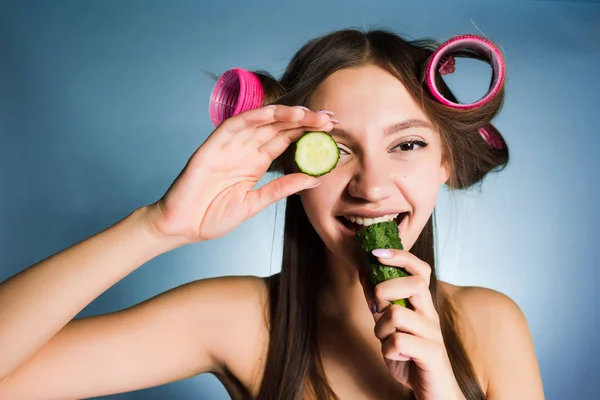 キュウリを食べる彼女の頭にカーラーで幸せな女 — ストック写真