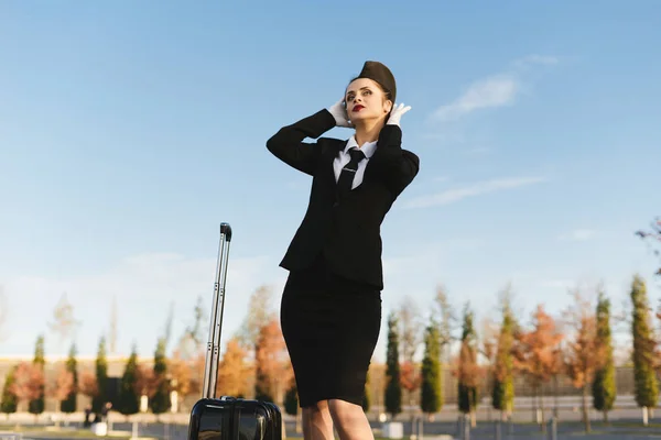 Nő stewardess egységes lelátókon mellett a háttérégbolt bőrönd — Stock Fotó