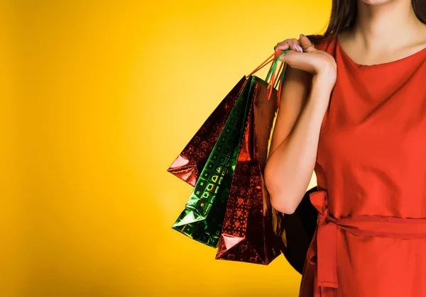 Женщина в красном платье держит в руках сумки для покупок на желтом фоне — стоковое фото