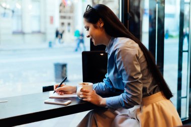 güzel mavi gömlekli mutlu kız serbest meslek sahibi bir şey bir not defterinde yazıyor kahve bir kafede içecekler