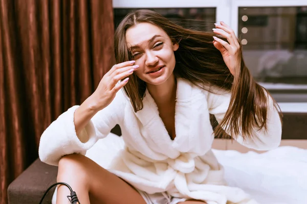 Lachendes junges Mädchen in weißem Gewand auf dem Bett sitzend, lange Haare — Stockfoto