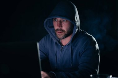 bir kazak bir masada oturan ve laptop arıyorum bir kukuleta ile erkek hacker