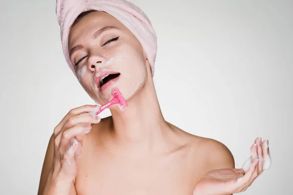 Donna con un asciugamano sulla testa dopo una doccia fa una depilazione del viso con un rasoio — Foto Stock