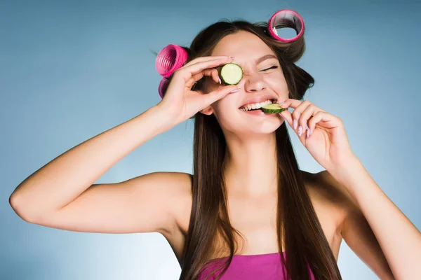 Lycklig kvinna med papiljotter på hennes huvud äta gurka — Stockfoto