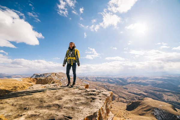 Женщина турист с большим рюкзаком стоит на краю скалы на фоне высоких гор — стоковое фото