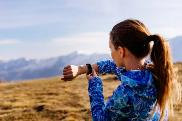 Kvinna turist tittar på fitness armband på bakgrund av berg — Stockfoto