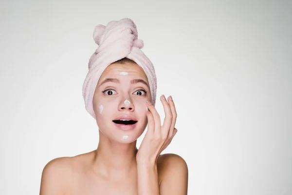Изумленная женщина с полотенцем на голове после душа нанесите на крем для лица — стоковое фото