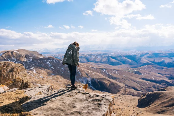 Turista mujer de pie en el borde de un acantilado en el fondo de las altas montañas —  Fotos de Stock