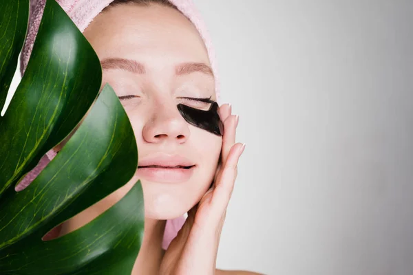 A woman holding a large leaf put on her face black patches — Stock Photo, Image