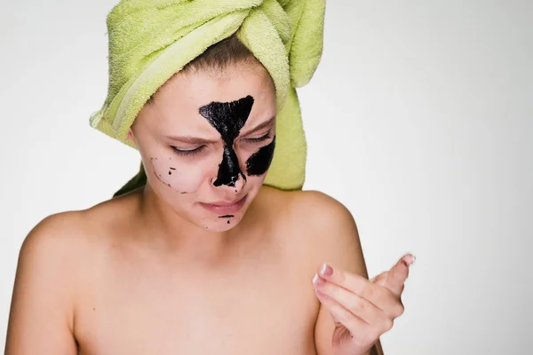 A woman with a towel on her head removes the mask from her face — Stock Photo, Image