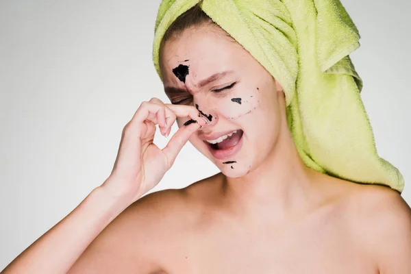 A woman with a towel on her head removes the mask from her face — Stock Photo, Image