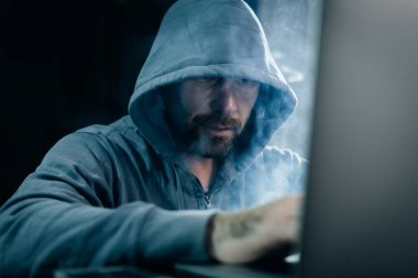 oturma ve karanlık bir odada dizüstü bakarak bir kukuleta ile bir kazak erkek hacker