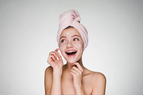 Femme heureuse avec une serviette sur la tête appliquer de la crème sur la peau du visage — Photo