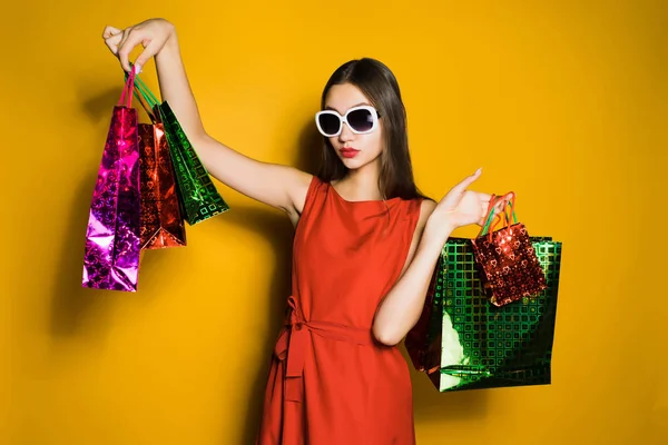 Женщина в очках стоит на желтом фоне с покупками в руках — стоковое фото