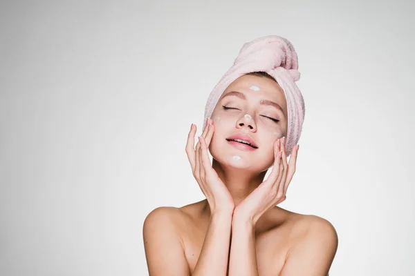 Женщина с полотенцем на голове намазывает крем на лицо — стоковое фото