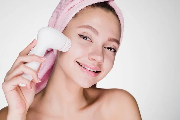 Femeia uimită cu un prosop pe cap după duș curăță pielea cu o perie pentru curățarea profundă a feței — Fotografie, imagine de stoc