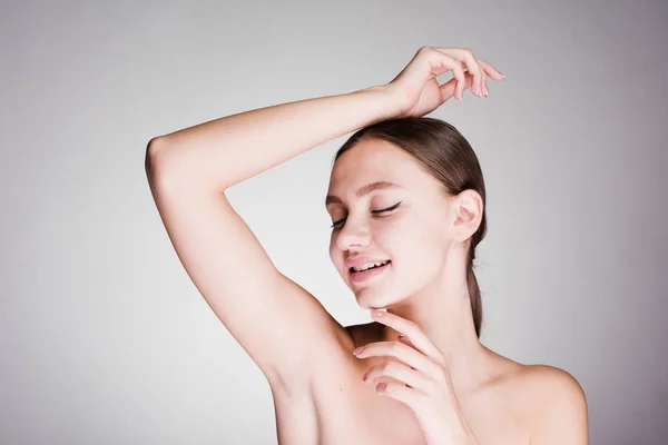 Astonished woman cares for the underarm skin on a gray background — Stock Photo, Image
