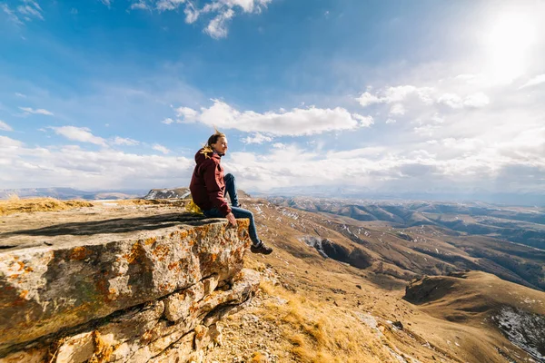 Mulher feliz turista senta-se em um penhasco no fundo das montanhas — Fotografia de Stock