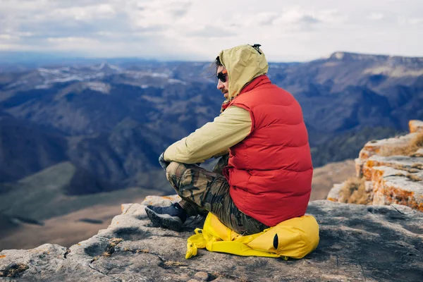 Mužské turistické sedí na vrcholu útesu na pozadí hor — Stock fotografie